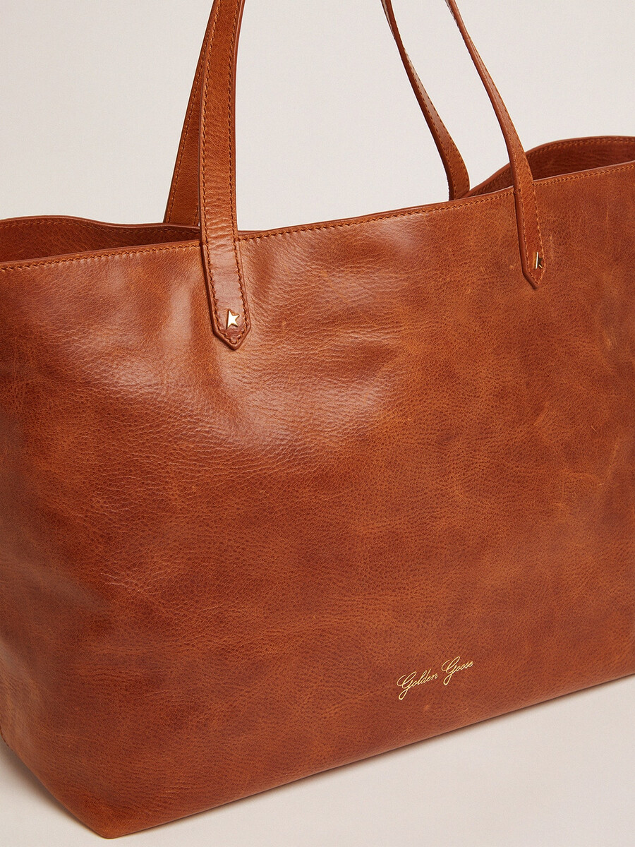 bolsa pasadena em couro martelado brilhante na cor bege com logotipo dourado na parte frontal.