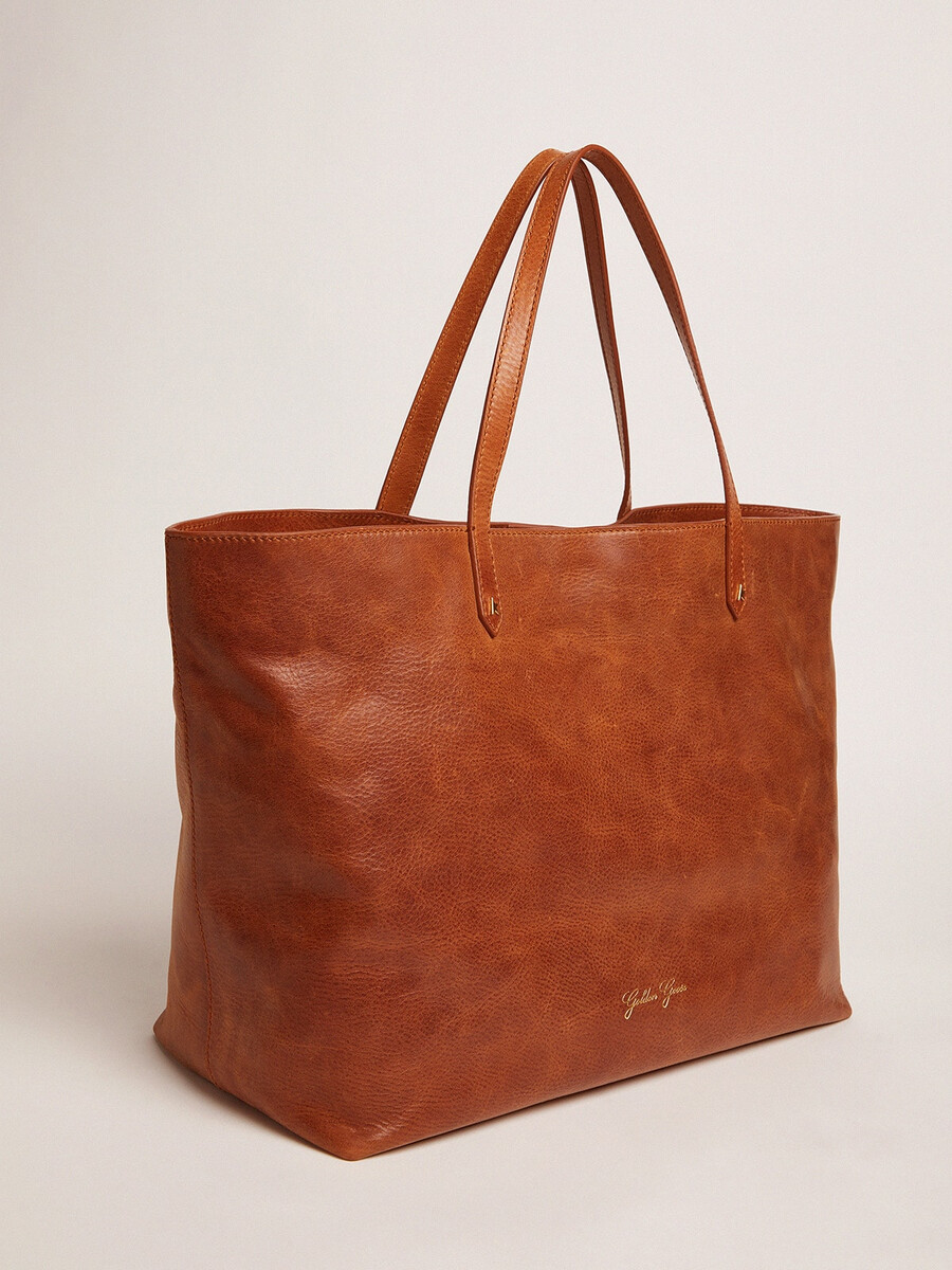bolsa pasadena em couro martelado brilhante na cor bege com logotipo dourado na parte frontal.
